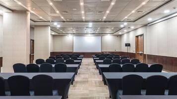 Un salón de conferencias con filas de mesas y sillas, una pantalla de proyector y una puerta de madera.