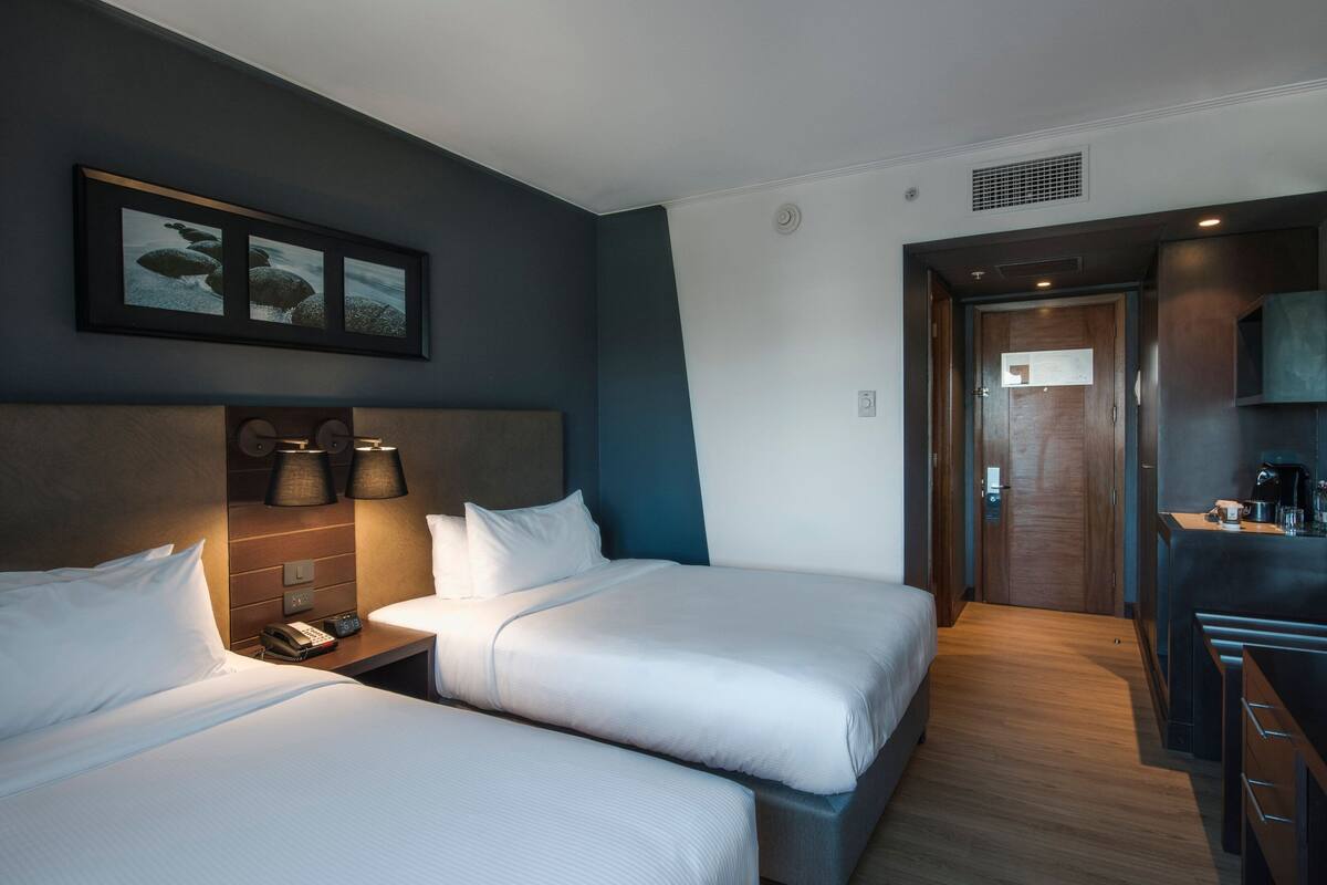 Ein Hotelzimmer mit zwei Betten, einer kleinen Küchenzeile und einem gerahmten Bild an der Wand.