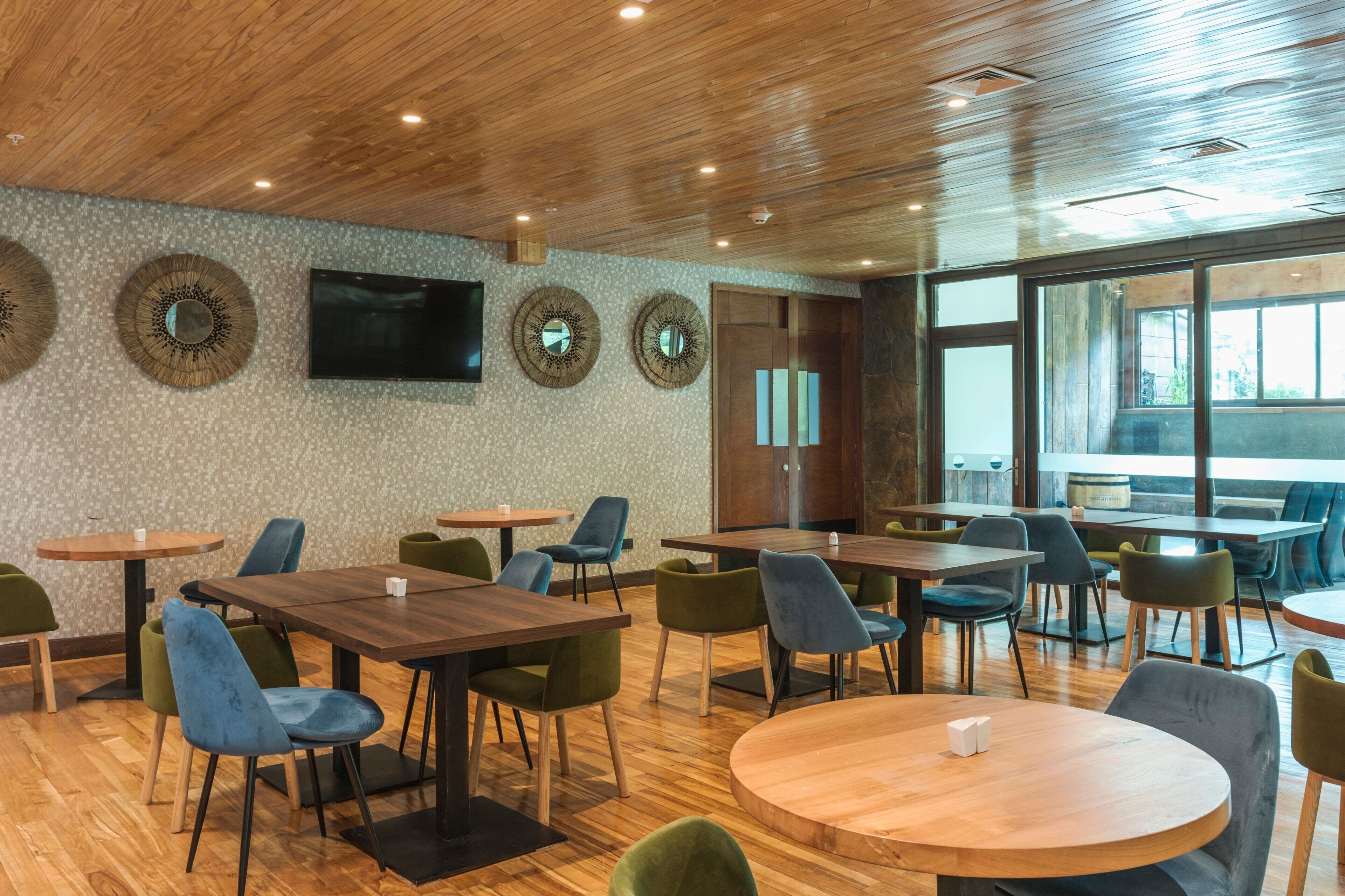 A modern dining area with wooden tables and chairs, a flat-screen TV, and large windows.