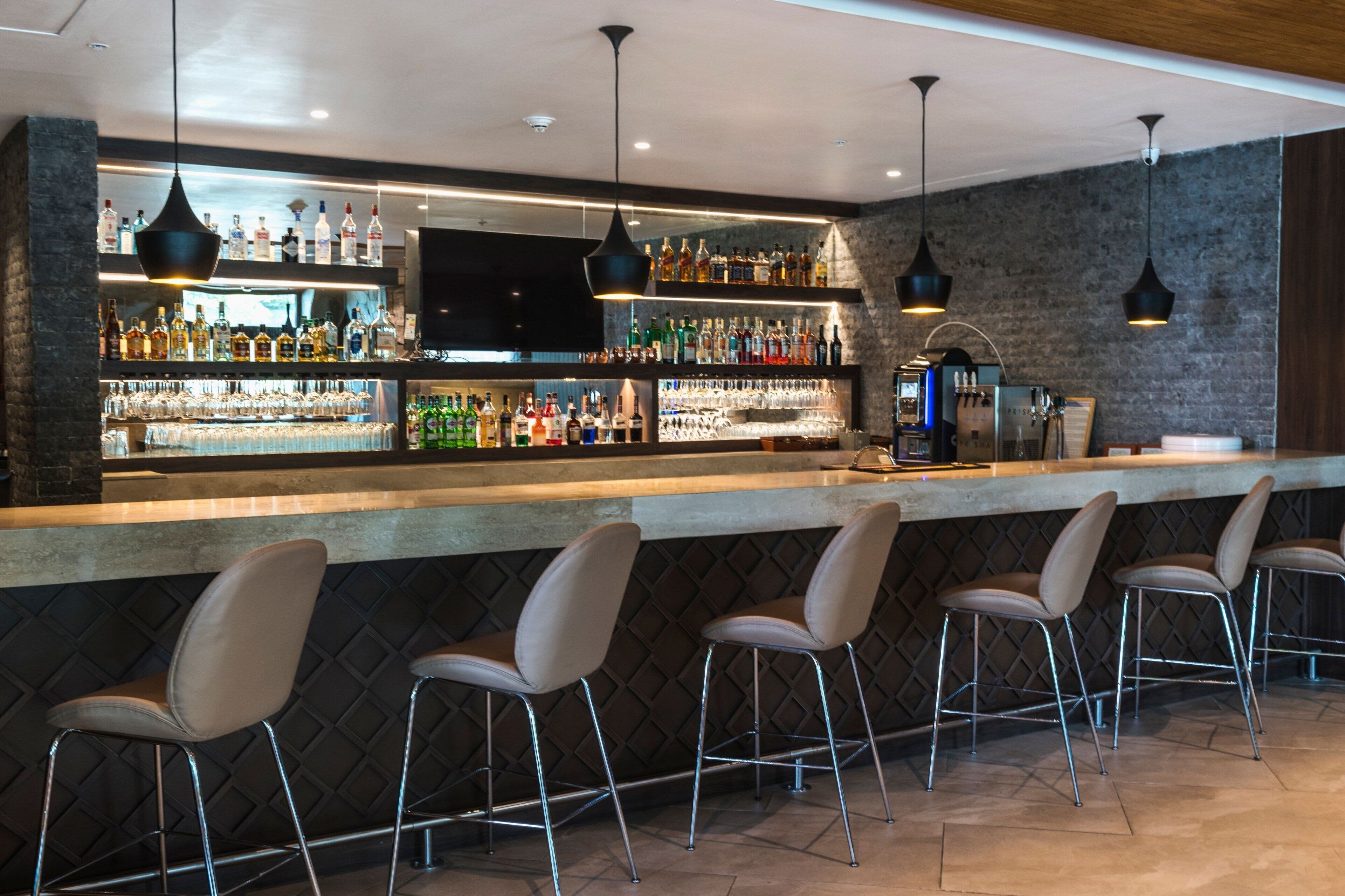 A bar area with a long counter, multiple shelves of bottles, and bar stools.