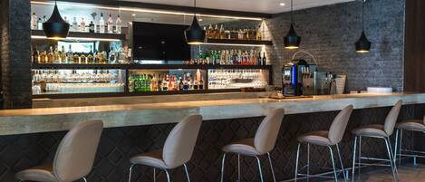 A bar area with a long counter, multiple shelves of bottles, and bar stools.
