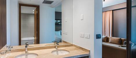 A modern bathroom with a double sink, a mirror, and a shower area visible through an open door.