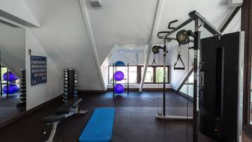 Uma academia com equipamentos de exercício, um tapete azul e janelas amplas.