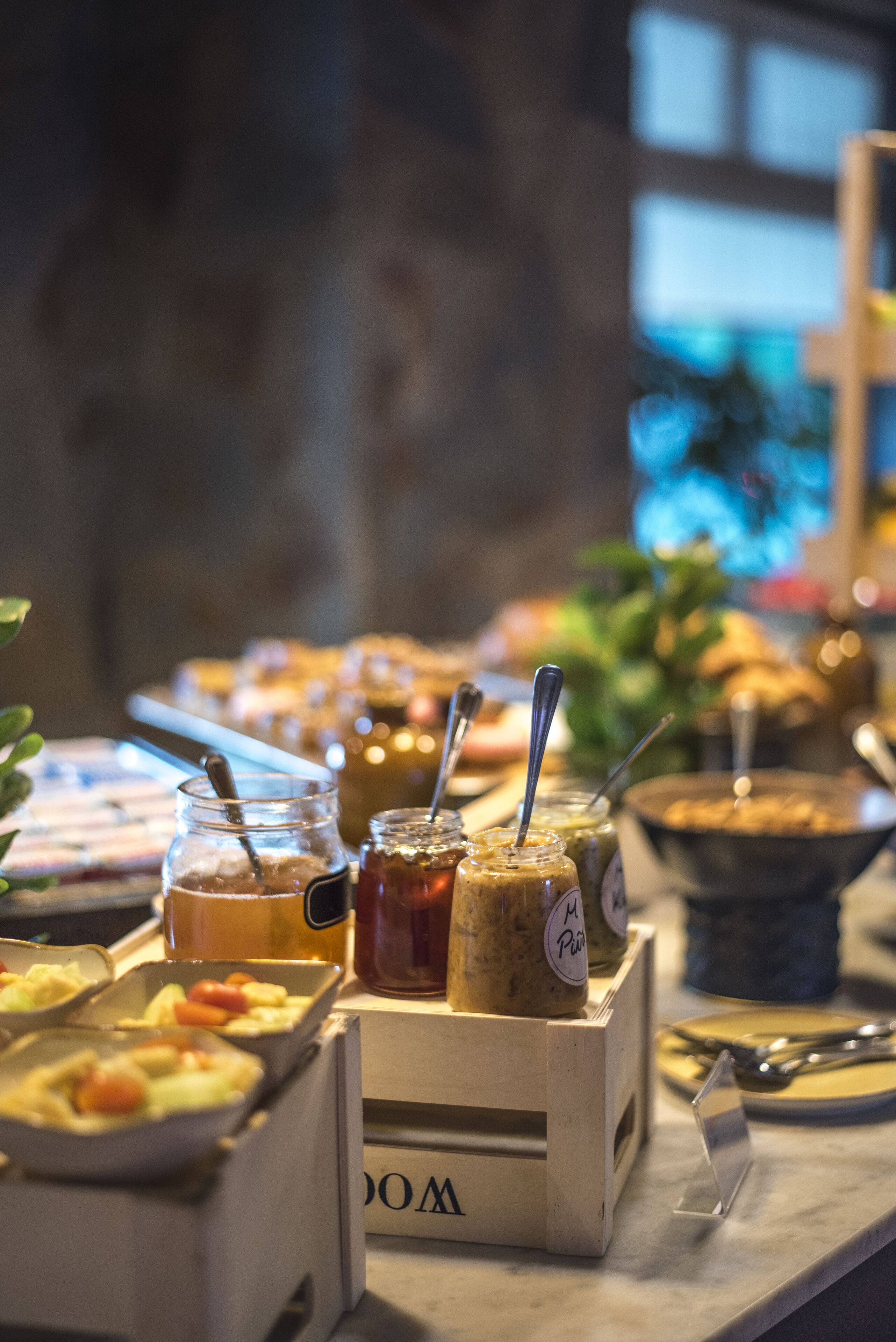 Un bufé con diferentes alimentos y acompañamientos, incluyendo frascos de salsas y un tazón de sopa.