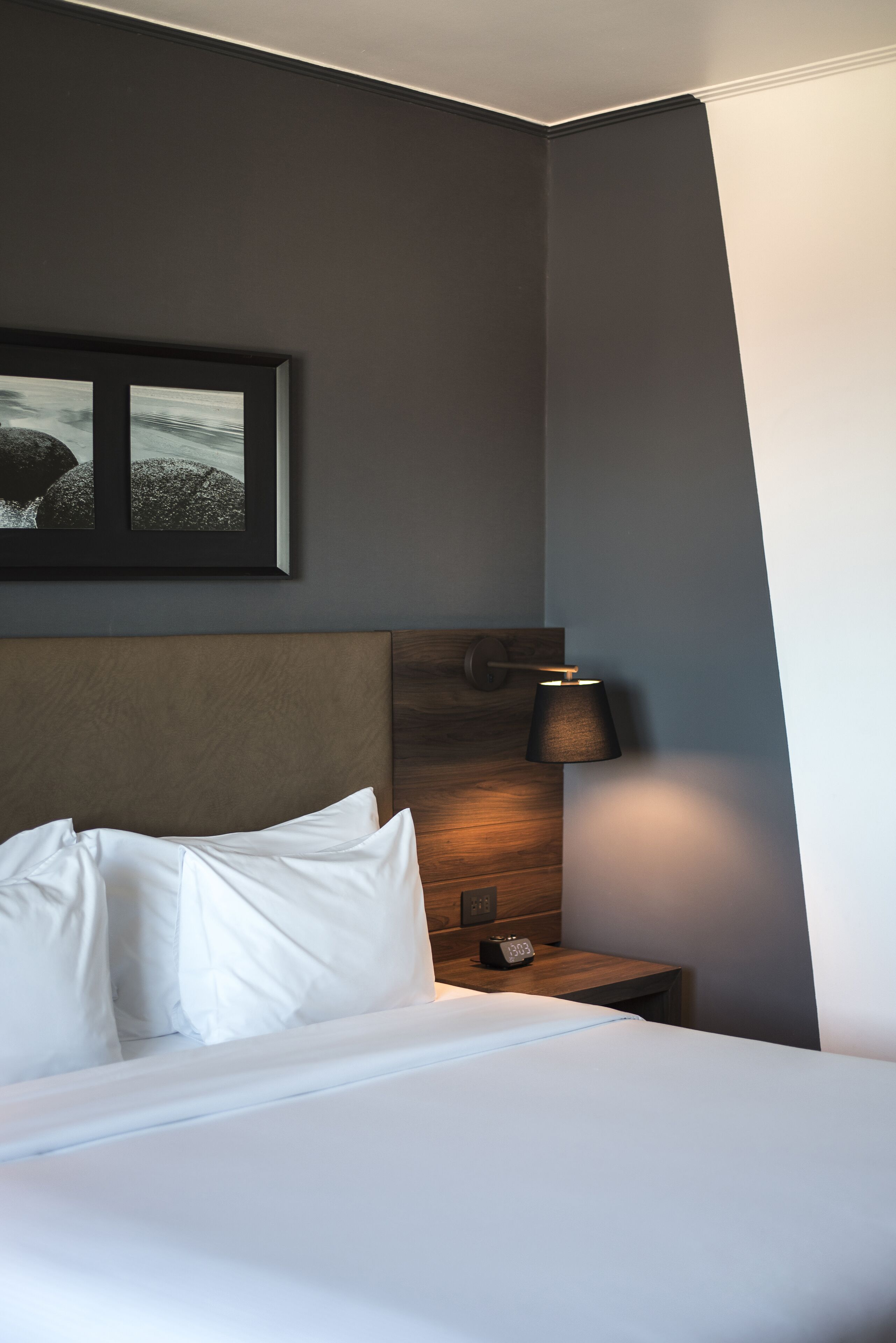 A neatly made bed with white linens, a framed picture on the wall, and a bedside table with a lamp and a radio.