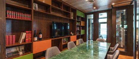 Une salle de conférence moderne, dotée d’une table en marbre vert, d’étagères en bois où sont rangés des livres et des bouteilles de vin, et d’un grand téléviseur à écran plat.