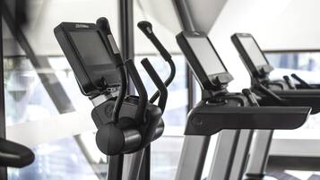 A row of stationary bikes with digital screens, positioned in front of a large window.