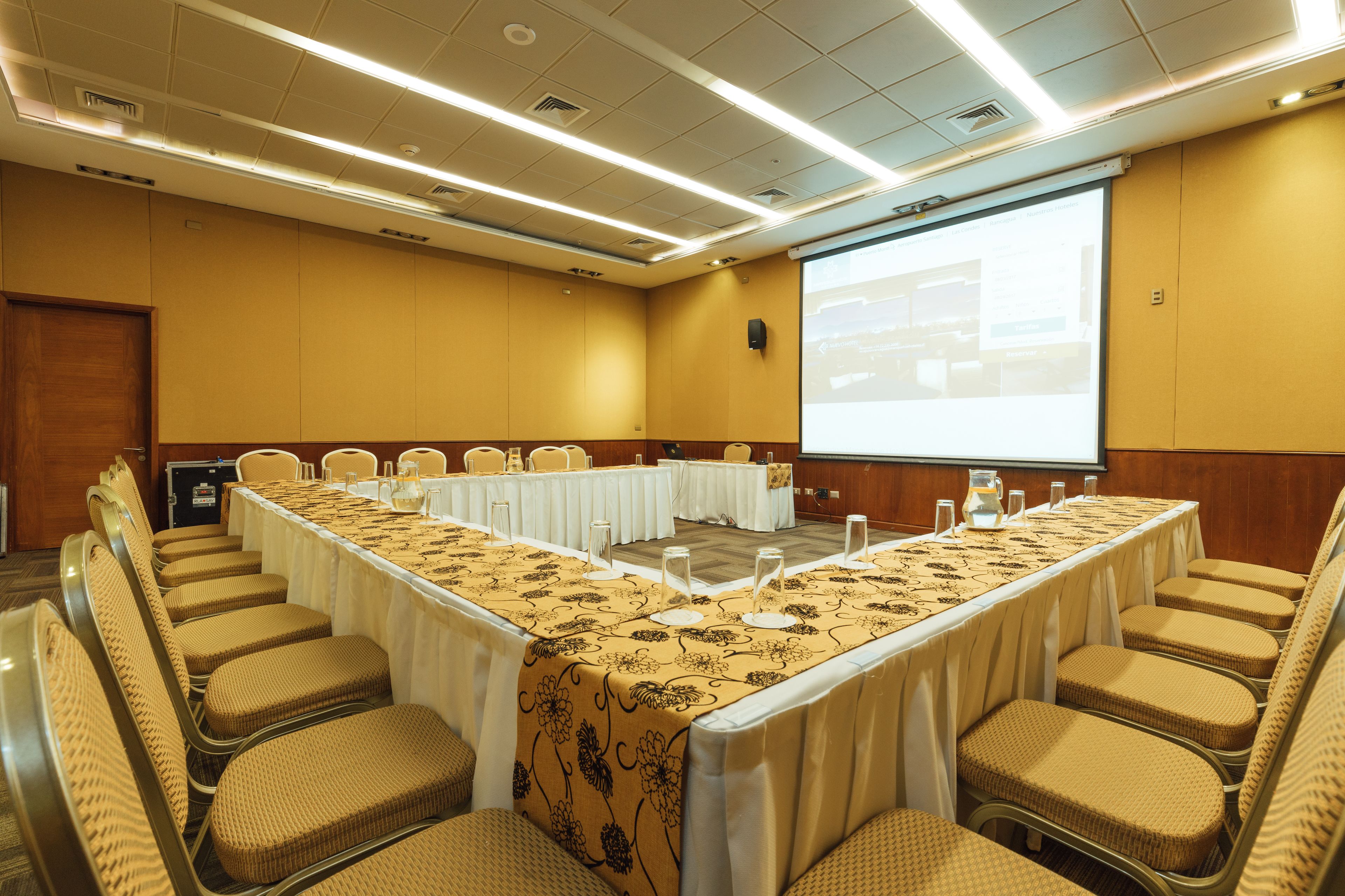 A conference room with a long table, multiple chairs, a projector screen, and a presentation screen.