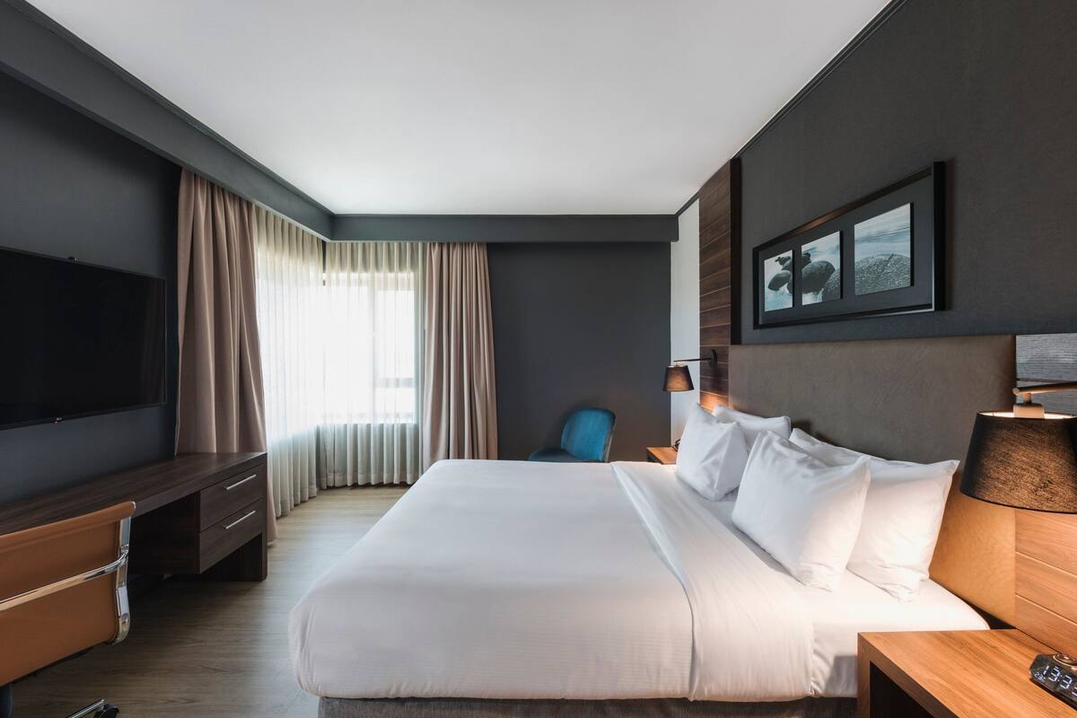 Ein modernes Hotelzimmer mit einem großen Bett, einem Flachbildfernseher, einem Schreibtisch und einem Sessel.