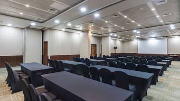 A conference room with rows of tables and chairs, a projector screen, and a carpeted floor.