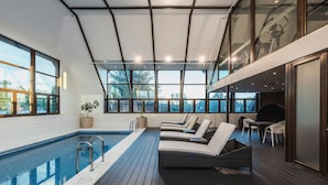 Piscina interior moderna con sillones de descanso y cubierta de madera.