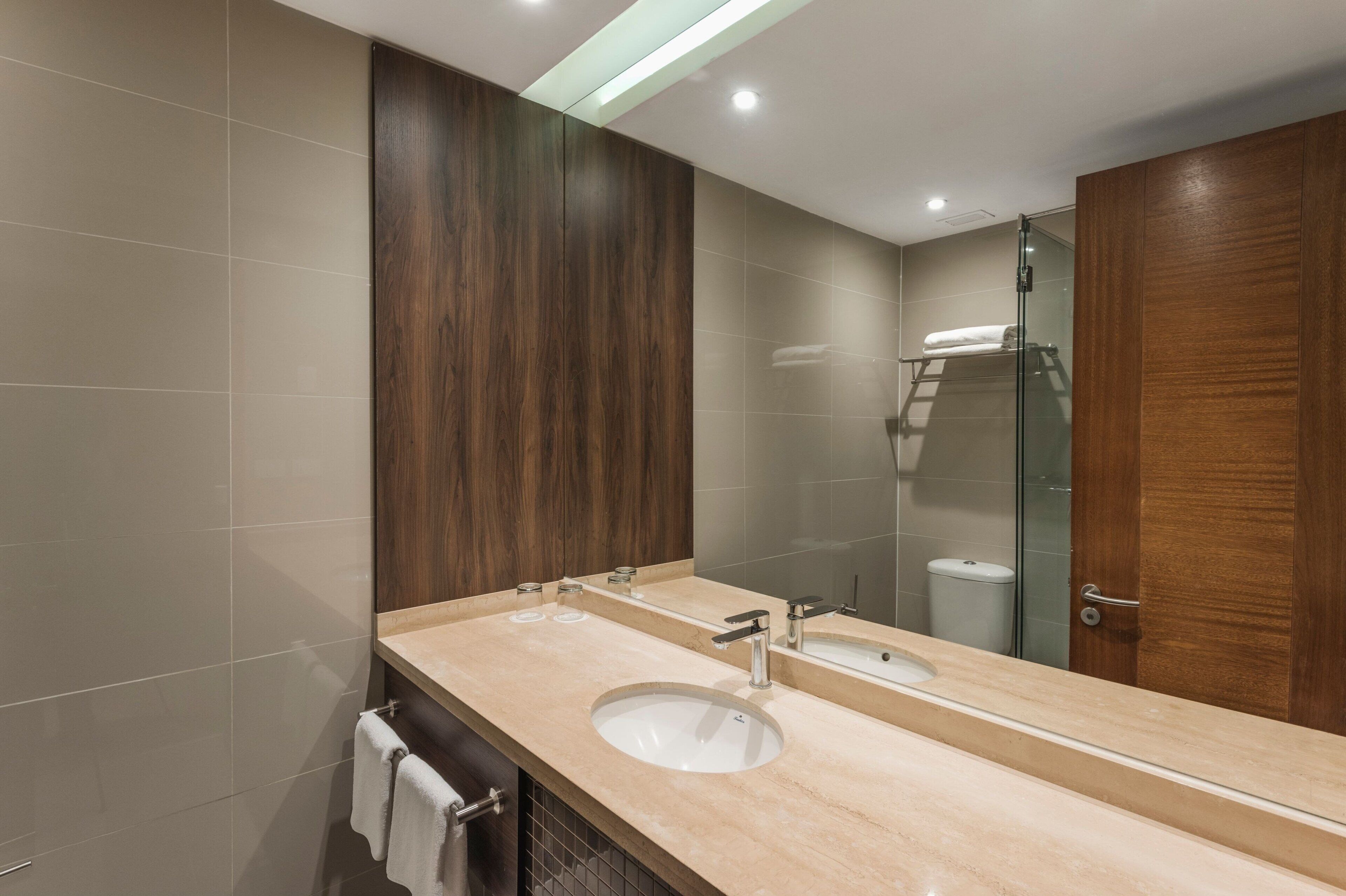 A modern bathroom with a large mirror, two sinks, and a glass shower enclosure.