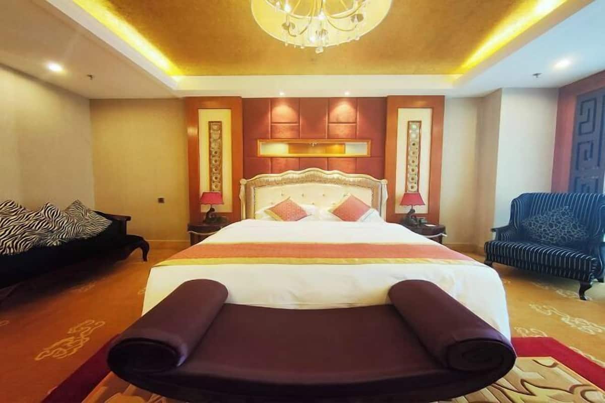 Une chambre d’hôtel avec un grand lit, une chaise longue, un canapé et un lustre.