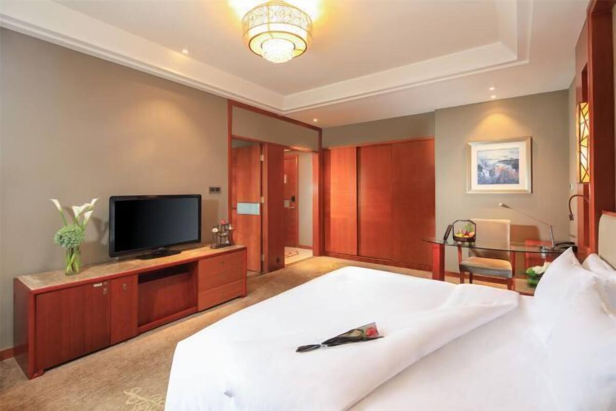 Une chambre d’hôtel comprenant un lit, une télévision, une armoire en bois et un bureau avec une chaise.