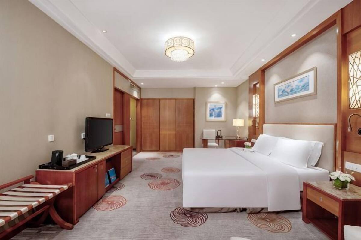 Une chambre d’hôtel comprenant un lit, un bureau avec une télévision, une lampe de bureau, une table de chevet et une œuvre d’art accrochée au mur.