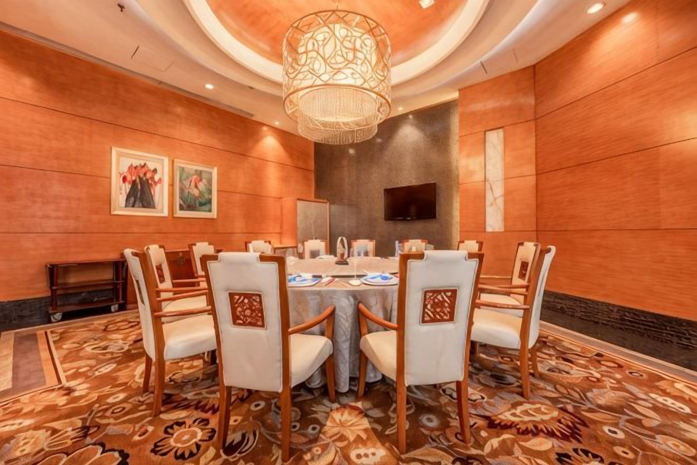 A conference room with a round table, chairs, a chandelier, and artwork on the walls.