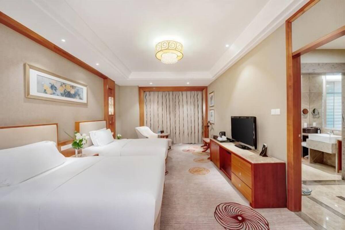 Une chambre d’hôtel avec deux lits, un bureau, une télévision et une salle de bain visible à travers une porte ouverte.