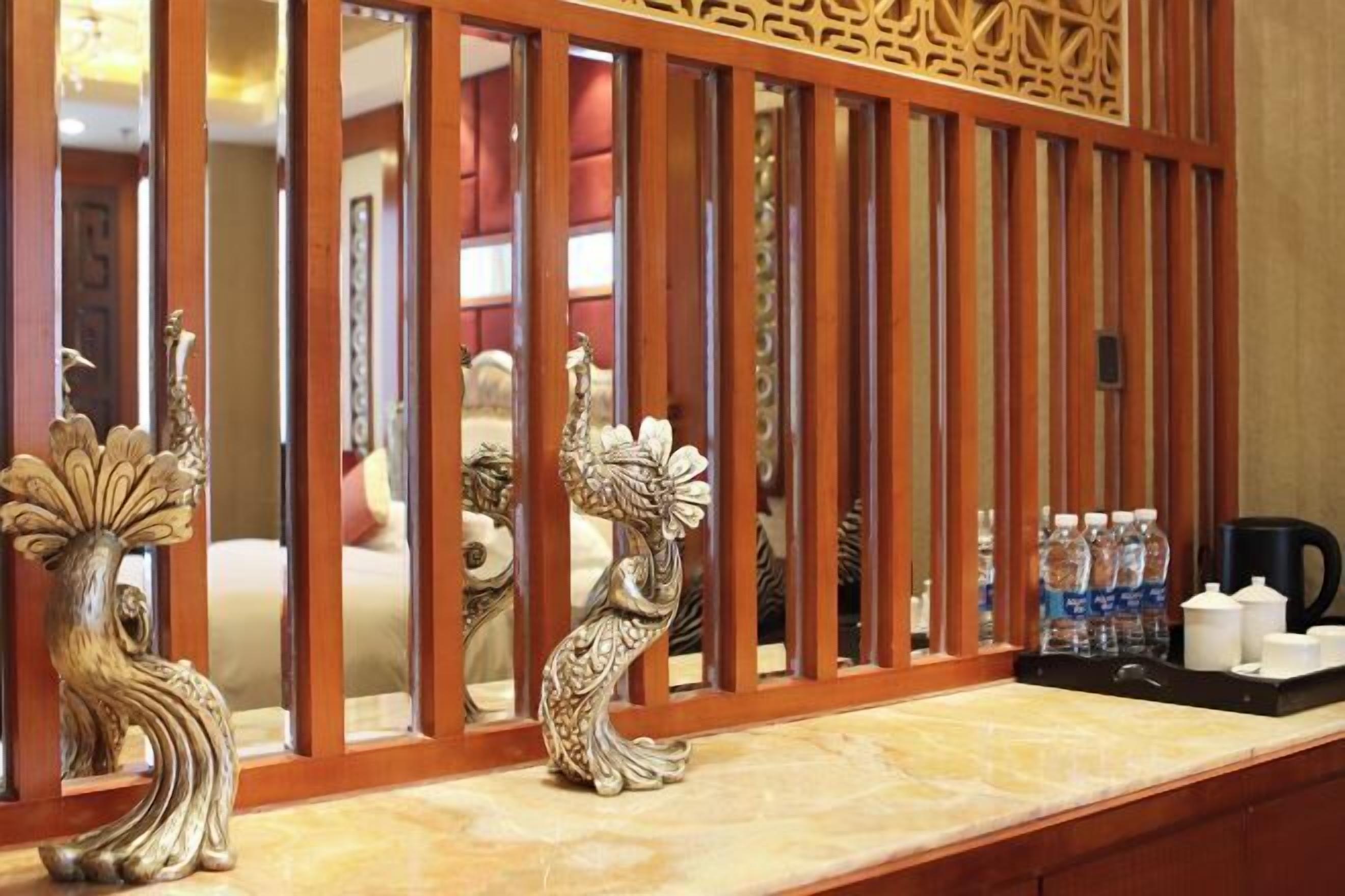 Zona de recepción de un hotel con un separador de madera, jarrones decorativos y una bandeja con botellas de agua y una máquina de café.