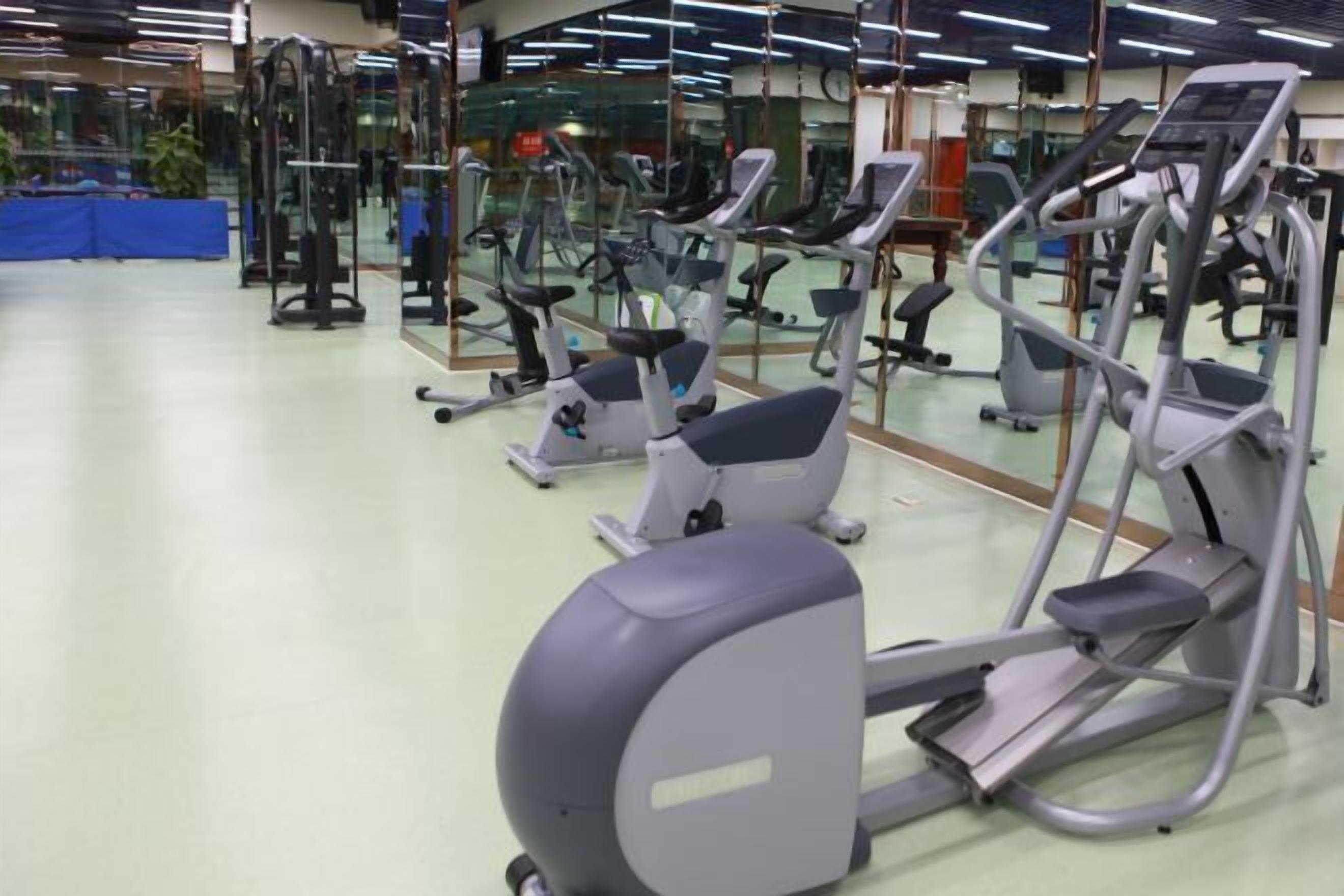A gym with various exercise machines, including treadmills and elliptical trainers, arranged in rows.