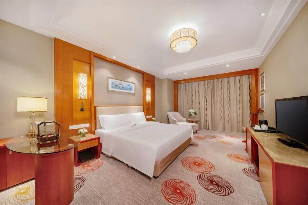 Une chambre d’hôtel avec un grand lit, un bureau avec une lampe, une chaise, une télévision et un panneau décoratif au mur.