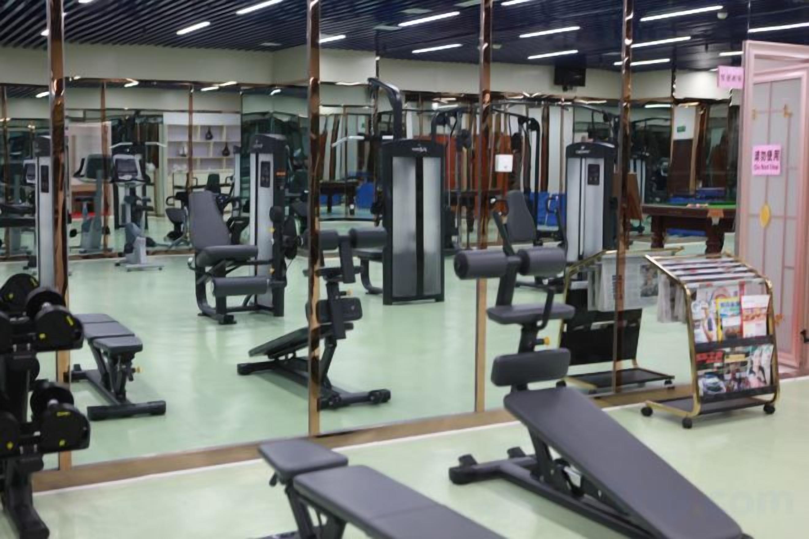 Un gimnasio con equipo de ejercicio diverso, espejos y un atril con revistas.