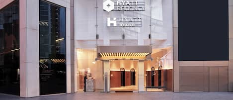 The exterior of a hotel with a modern design, featuring a prominent sign for the hotel and a reception area.