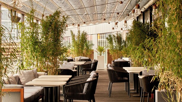 Un restaurante interior con suelo de madera, muebles de mimbre negro y techo a rayas.