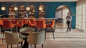 Zona de bar con asientos, un camarero y vistas del salón de reuniones y los baños del restaurante.