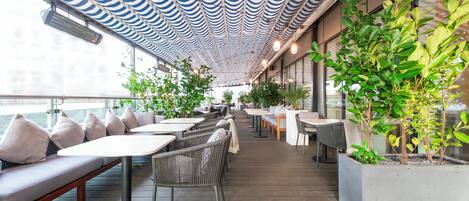 An outdoor seating area with tables and chairs, a patterned ceiling, and potted plants.
