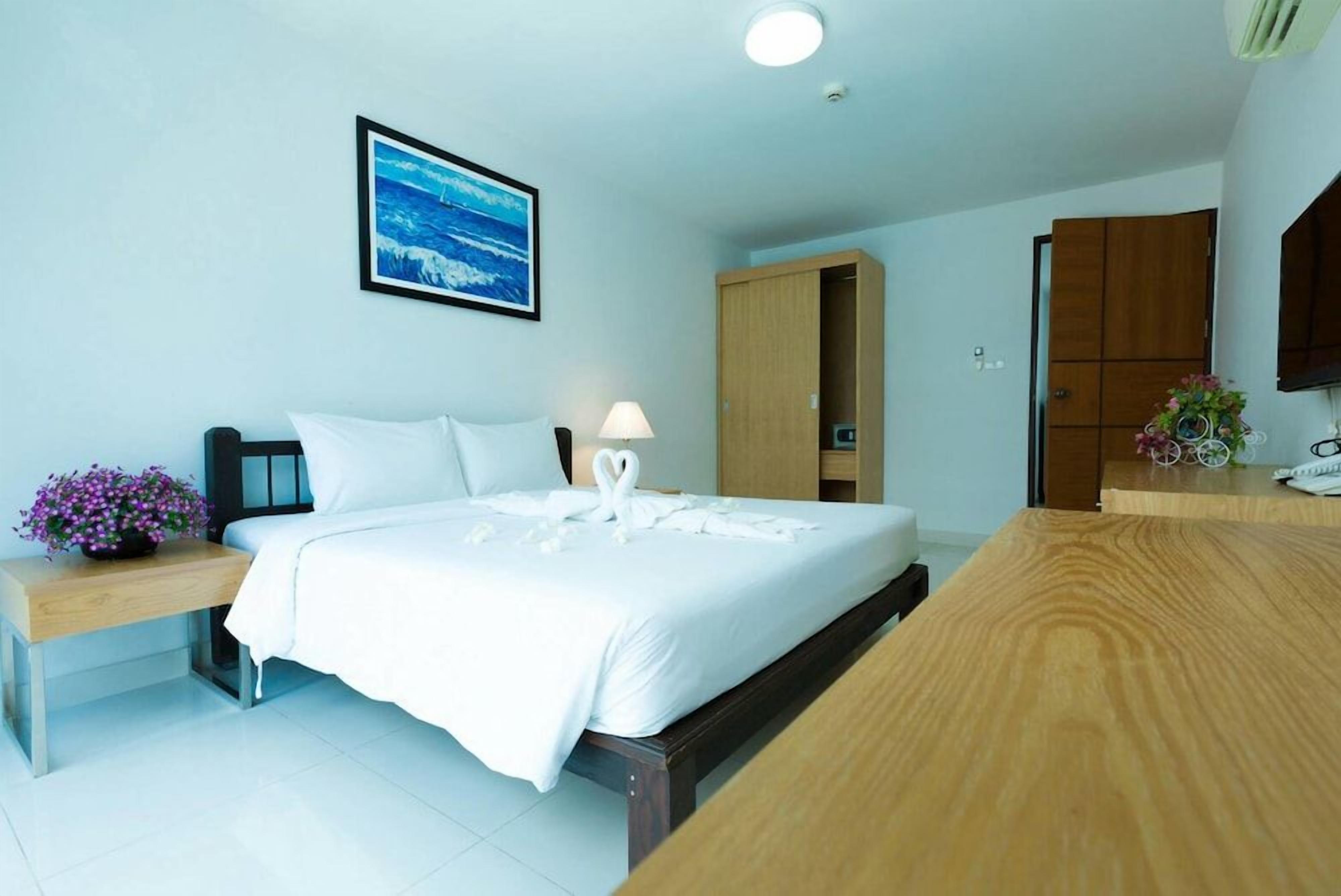 A hotel room with a bed, bedside table, lamp, and a framed picture on the wall.