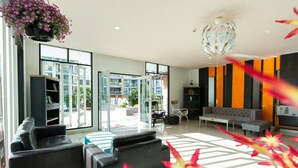 A modern living room with a sofa, armchairs, a coffee table, and a bookshelf. Large windows provide a view of the outside. - Neo Hotel Pattaya (Pattaya)
