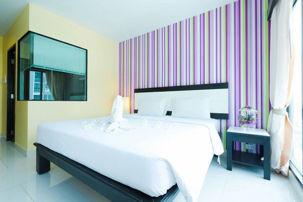 A modern hotel room with a large bed, a bedside table with a lamp, and a window with curtains.