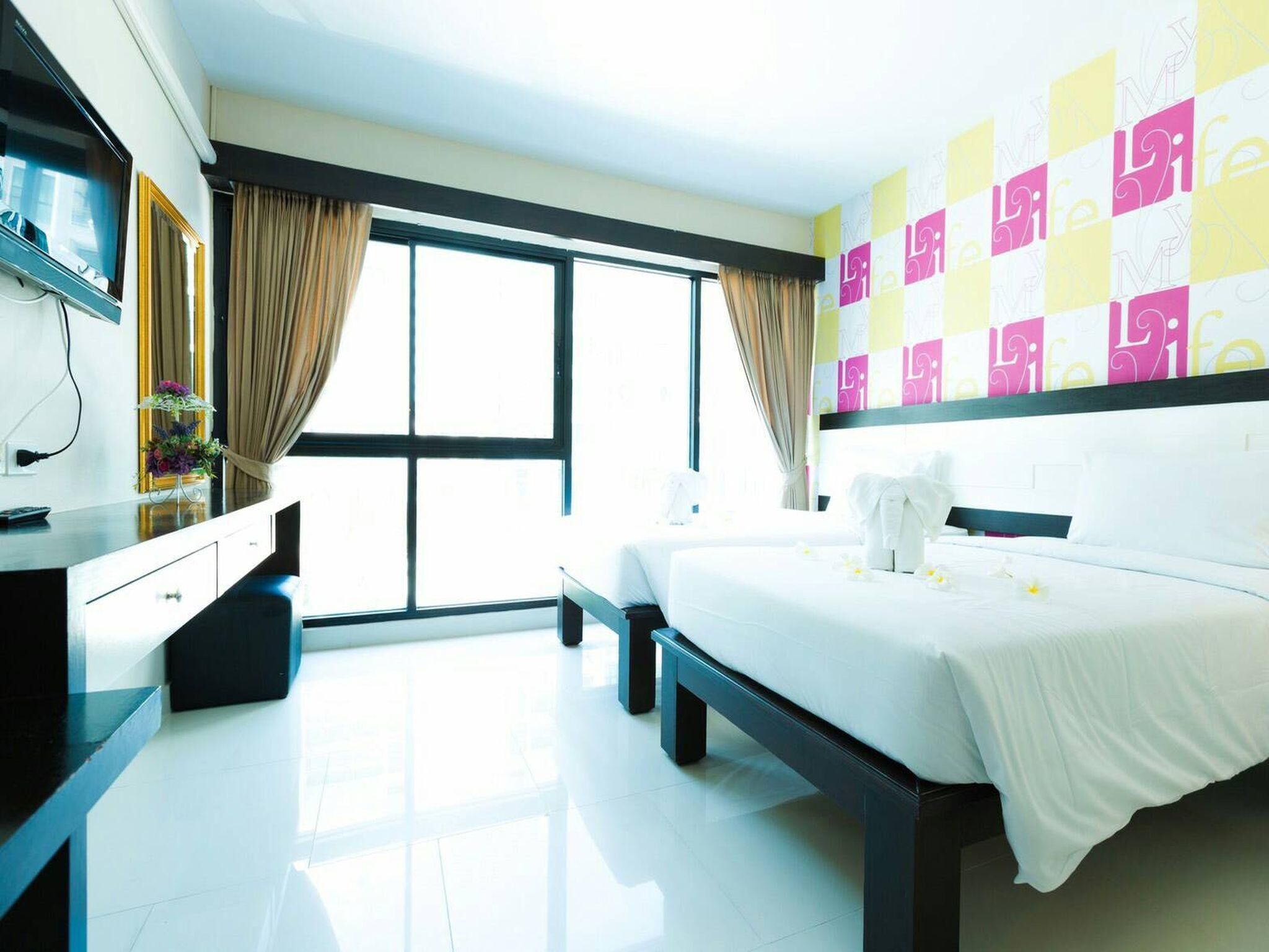 A modern hotel room with a large bed, a bedside table, a dresser, a mirror, and a window with curtains.