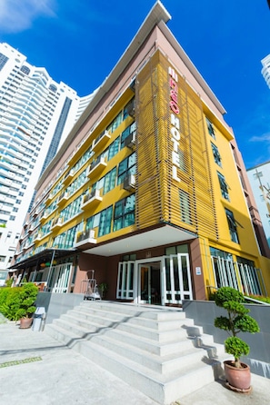 A hotel with a modern yellow facade, multiple balconies, and a clear view of the surrounding high-rise buildings.