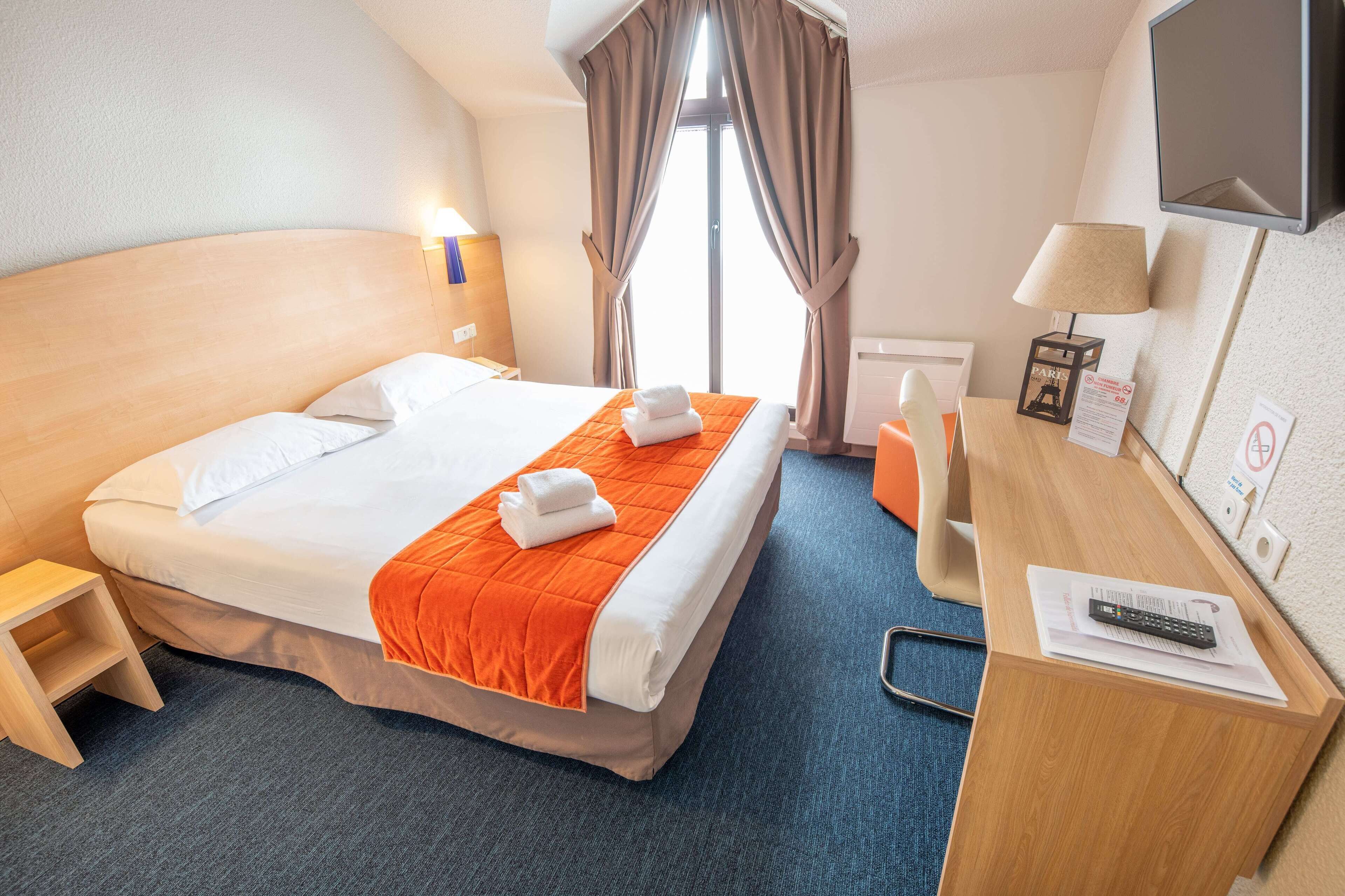 A hotel room with a bed, a desk, a chair, a TV, and a window with curtains.