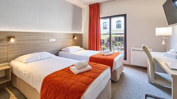 A hotel room with two beds, a desk, and a TV.