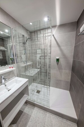 Une salle de bain moderne avec une douche à parois de verre, un lavabo blanc et un miroir.