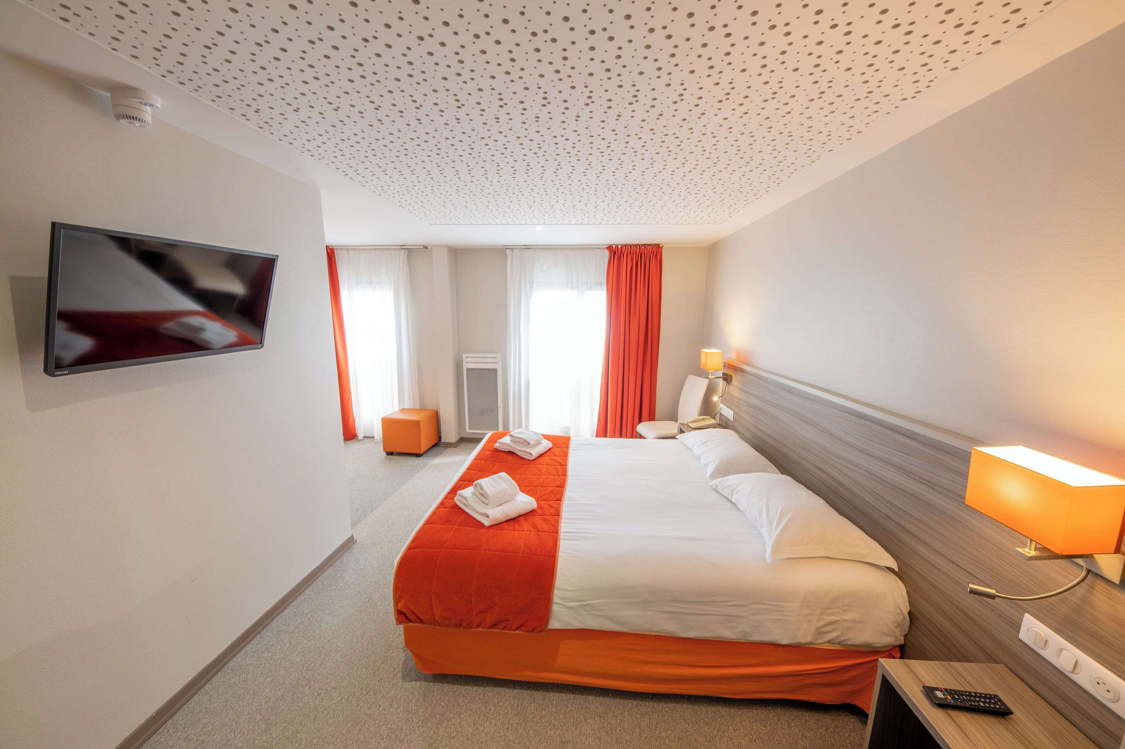 Quarto de hotel com cama, televisão, candeeiro e comando à distância.
