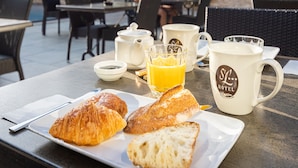 Un espace extérieur aménagé pour prendre les repas, avec des tables, des chaises et des parasols. On y trouve des croissants et une tasse sur la table.