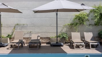 A poolside area with lounge chairs and umbrellas, a brick wall, and a pool.