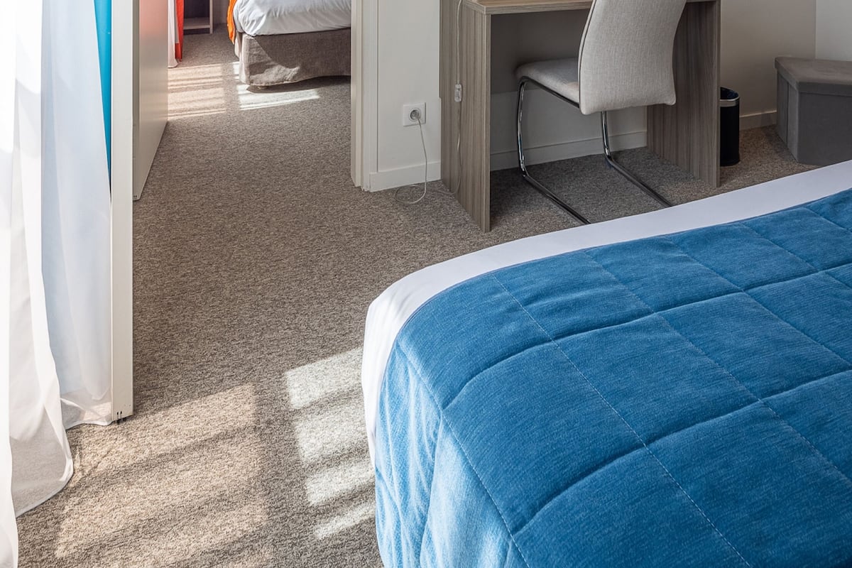A hotel room with a bed, a desk with a chair, a TV on the wall, and a door leading to another room.