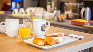 Una presentación para el desayuno con tazas de café, un vaso de jugo de naranja y pasteles sobre una mesa en una habitación de hotel.