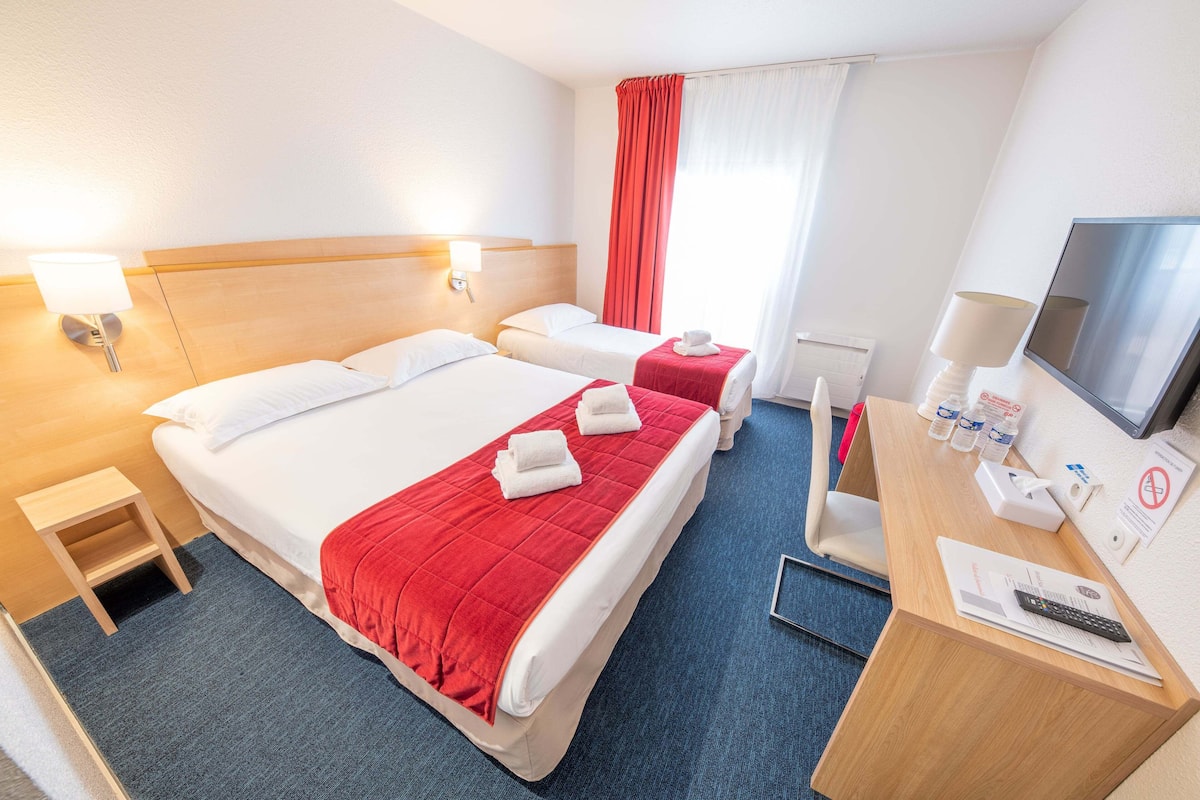 A hotel room with two beds, a desk with a TV, a lamp, and a small table.