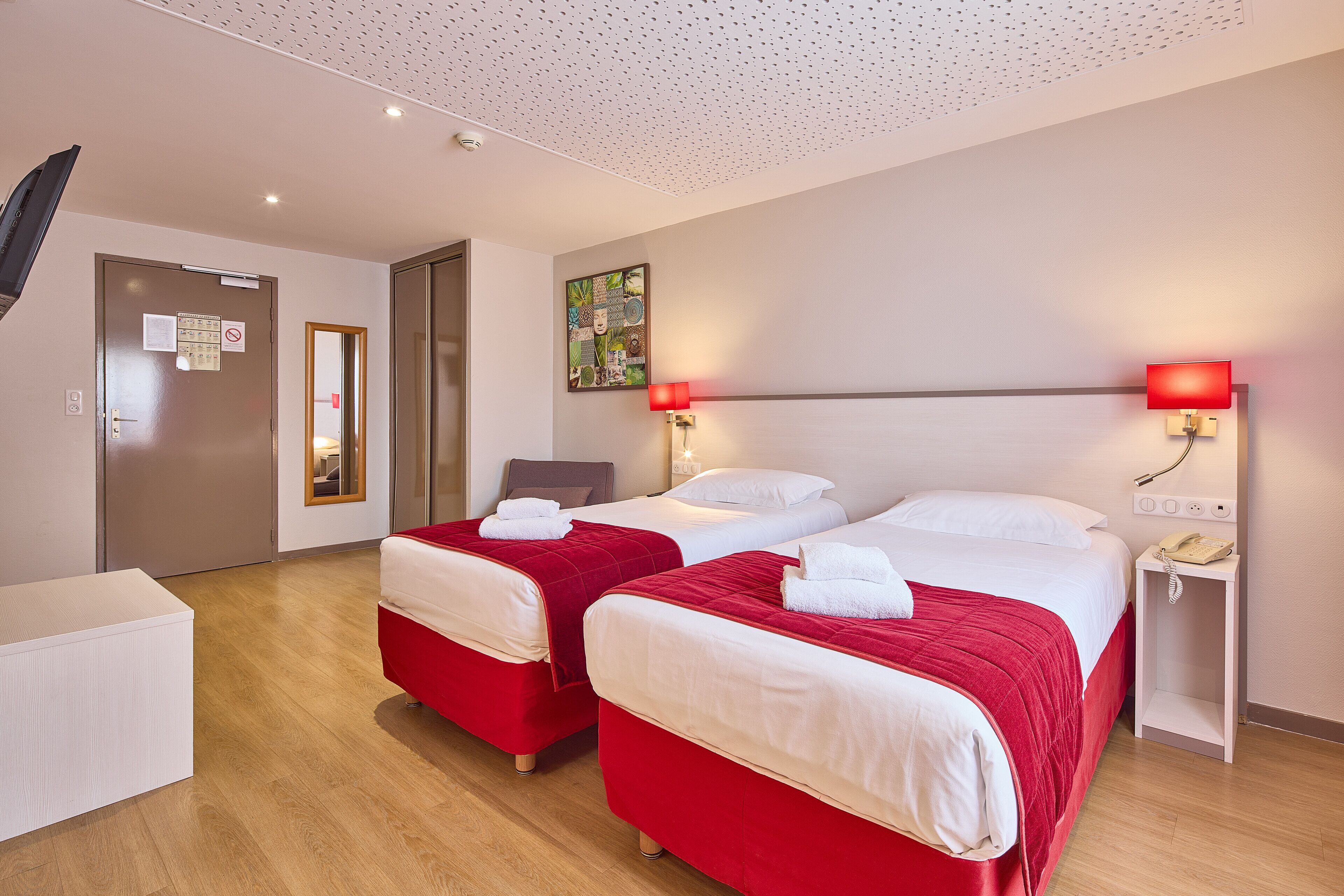Een hotelkamer met twee bedden, een bureau, een stoel, een telefoon en een kunstwerk aan de muur.