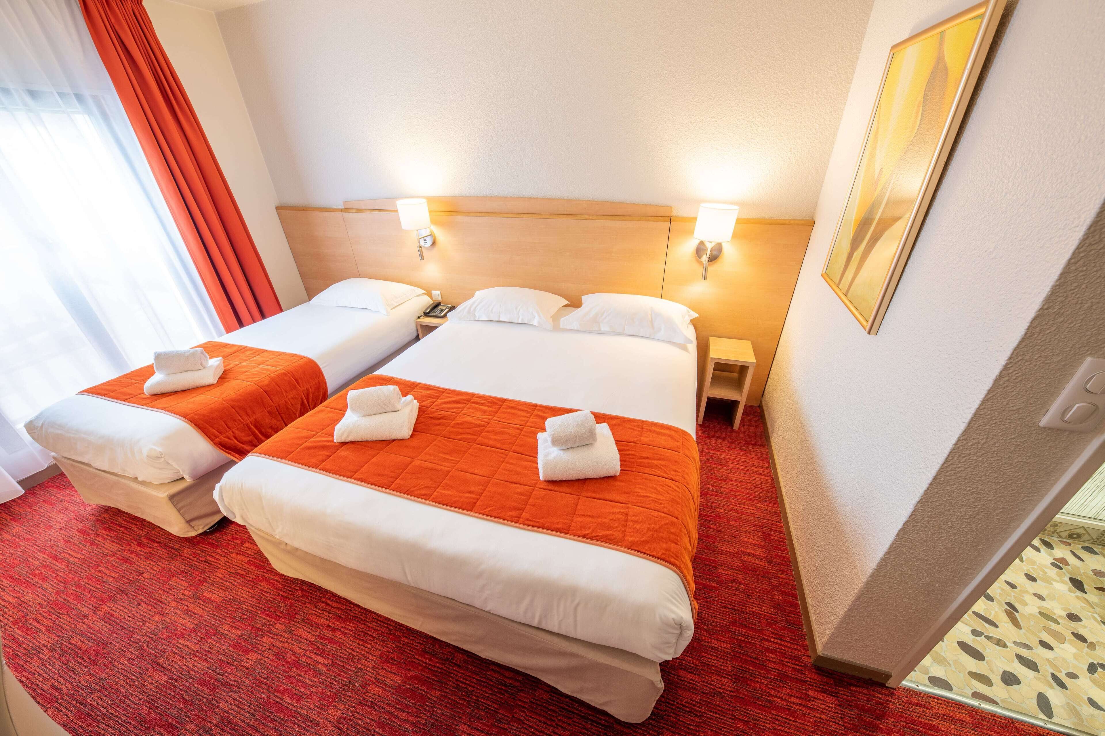 Habitación de hotel con dos camas, cada una con cubrecama naranja y almohadas blancas, y alfombra roja.