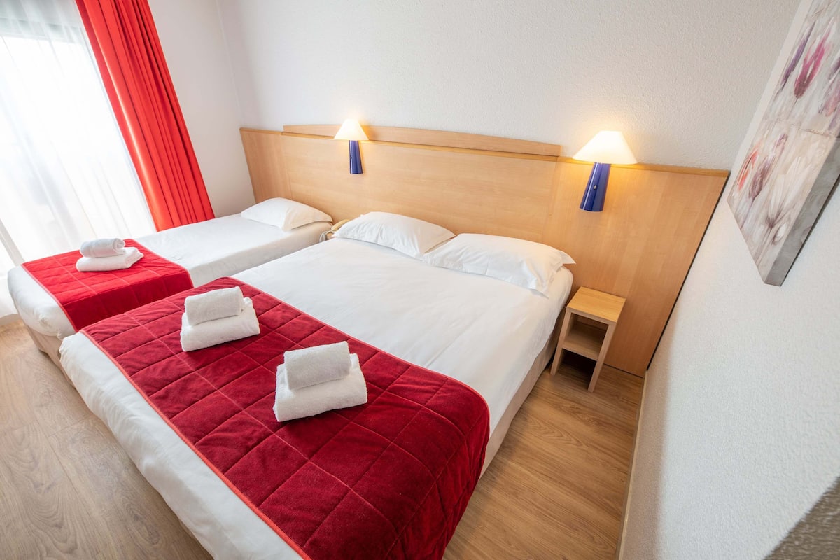 A hotel room with two beds, each with a red bedspread and white pillows, and two wall-mounted lamps.
