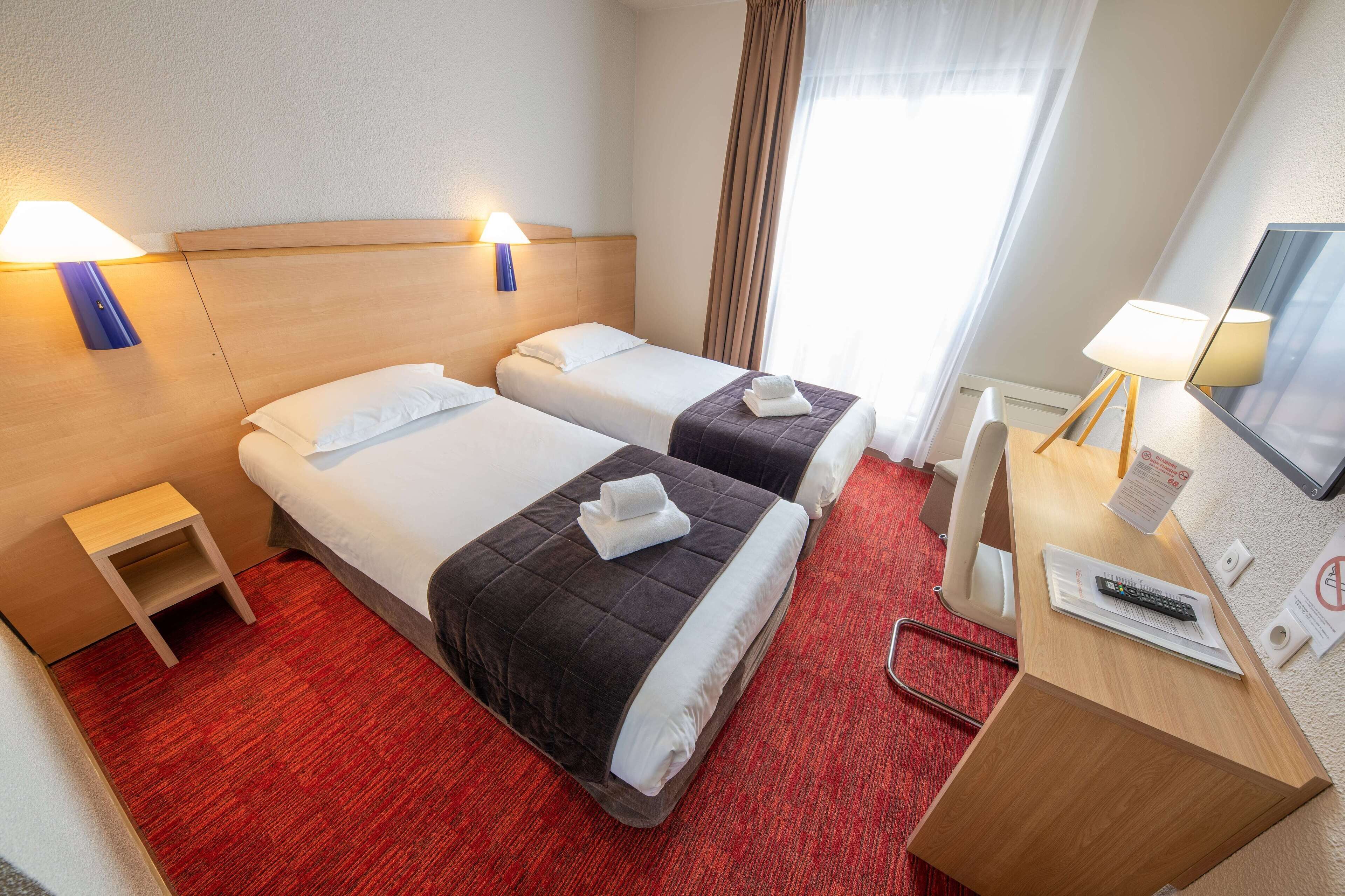 A hotel room with two beds, a desk with a computer, a TV, and a small table.