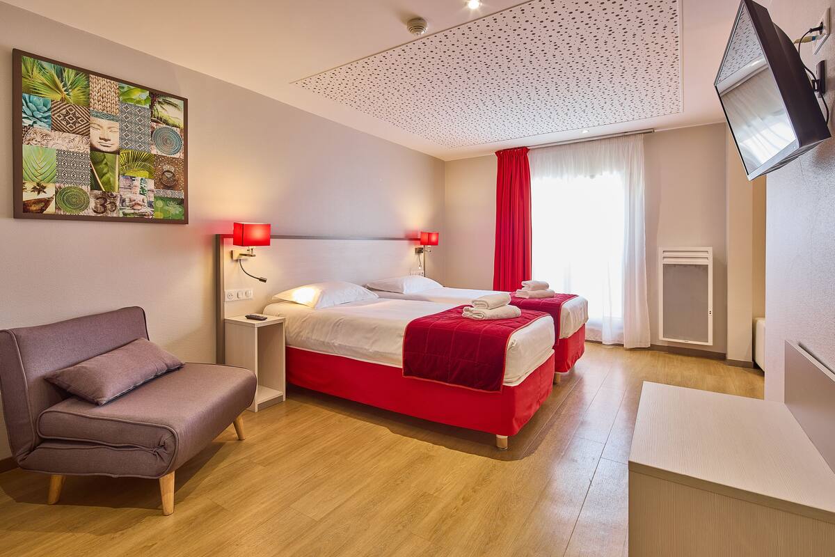 A hotel room with a bed, a sofa, a TV, and a wall art piece.