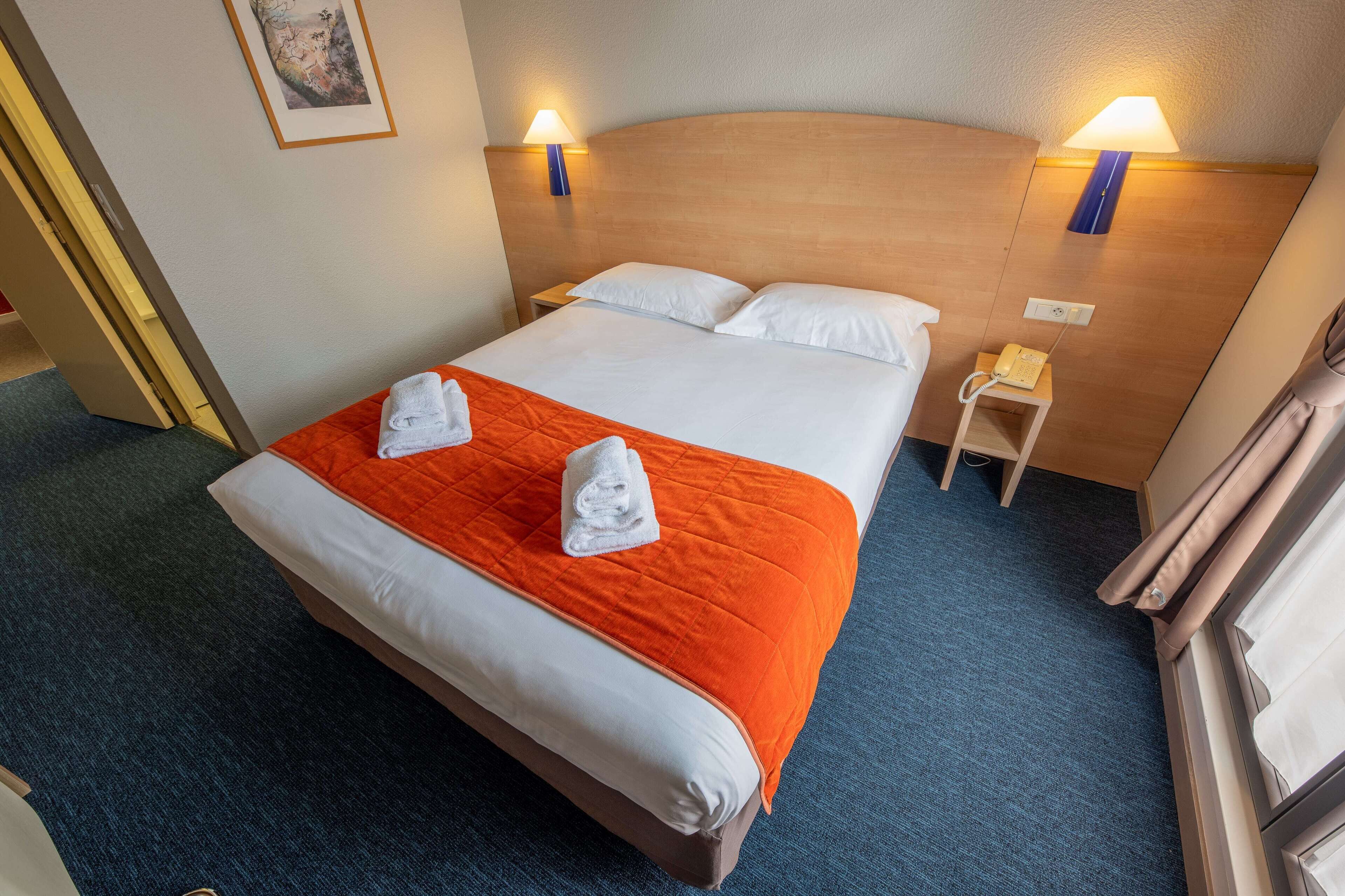 Habitación de hotel con una cama grande, dos lámparas de noche, un teléfono junto a la cama y una mesita pequeña.