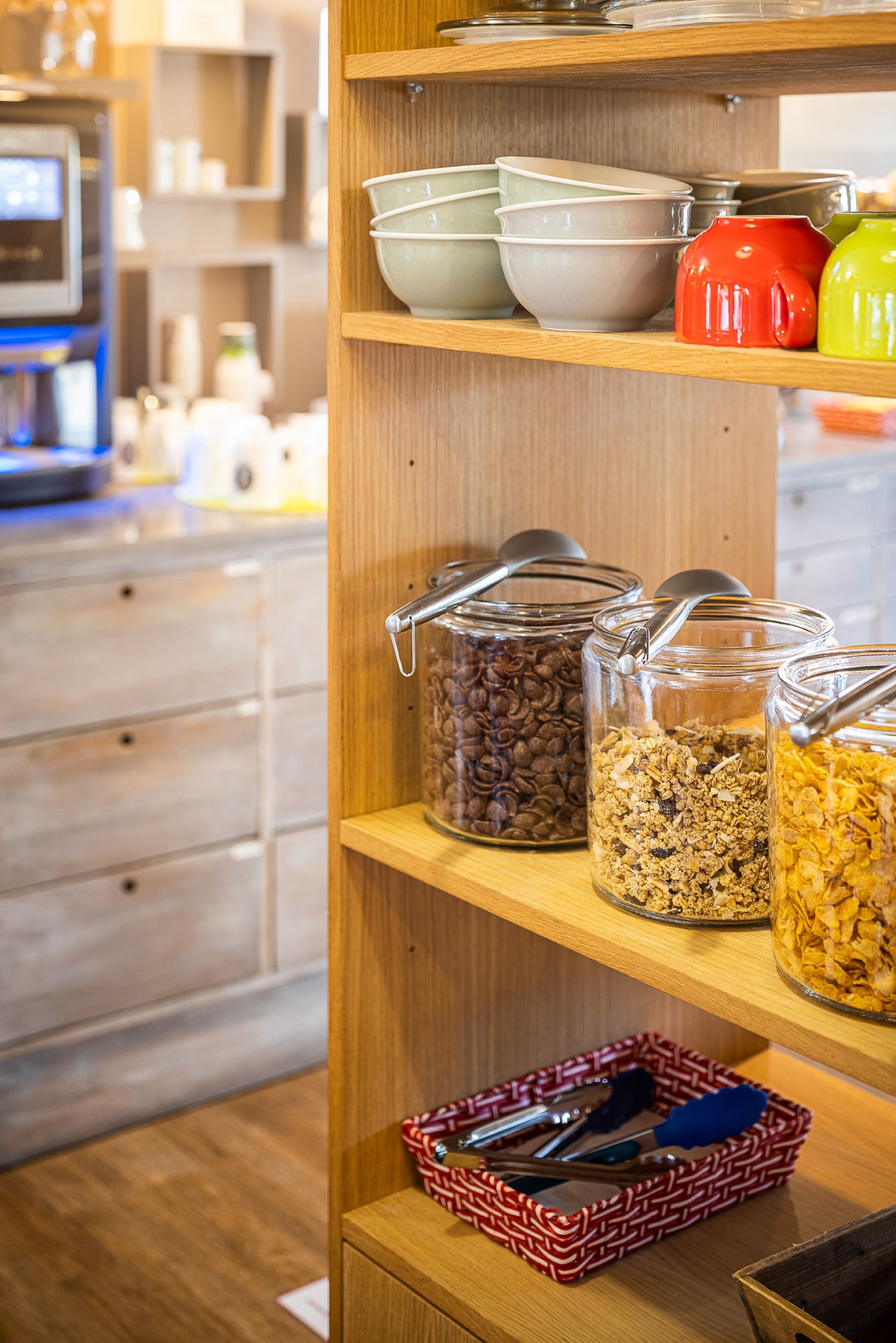 Un rincón de cocina con estantes de madera que exhiben tazones, frascos de granola y un cesto de utensilios.